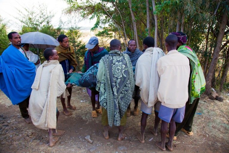 Men gather around a woman who has just had surgery to alleviate obstructed labor in preparation to carry her home. Motta, Ethiopia